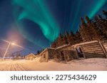 Incredible display of northern lights seen in winter season with old log style cabin. Huge green Aurora Borealis band seen dancing in the sky above. 
