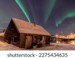 Incredible display of northern lights seen in winter season with old log style cabin. Huge green Aurora Borealis band seen dancing in the sky above. 