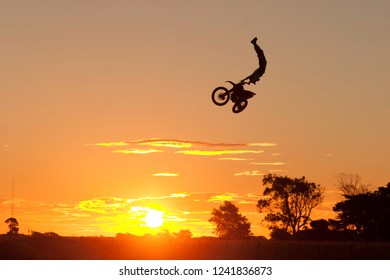 An Incredible Gymnastic Trick On A Motorbike On A Beautiful Sunset With Trees In The Background. The Rider Appears To Do An Almost Impossible Inverted Handstand While Being 10 Meters In The Air.