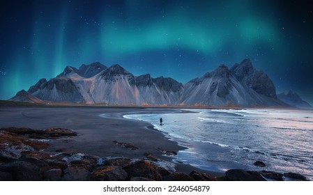 Incredible Iceland nature seascape. Iconic location for landscape photographers and bloggers. Scenic Image of Iceland. Alone tourist against Vestrahorn mountaine with Green northern lights - Shutterstock ID 2246054879