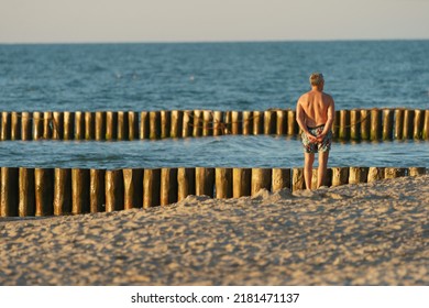 Incredible Soft Golden Sunset Over The Baltic Sea. The Sea Is Calm And Peaceful  Man Standing, Admiring View And Sunbathing. Concept Of Beauty. Lost In Nature. Back, Rear View