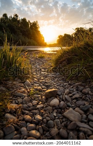 Incredibly beautiful sunset by the river. Rocky shore, trail leading to water. In the water surface reflected the sun's rays. Outdoor activities in summer, hiking to the river. High quality photo