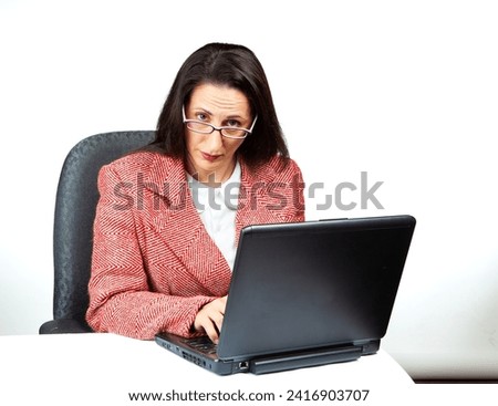 An incredulous woman in a tacky old business suit looks over her glasses from behind a laptop. Office concept showing contempt and bureaucracy