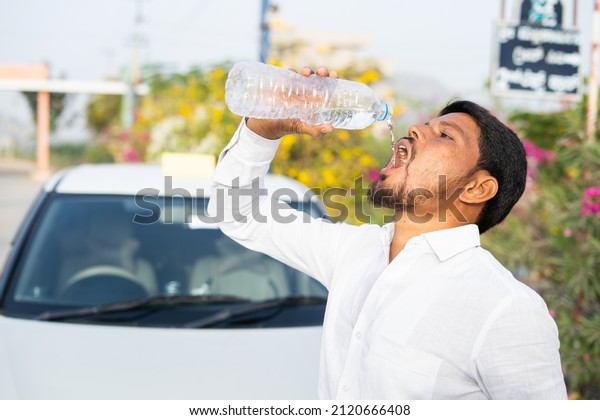 Indain cab driver drinking water while on\
front of car - concept of Healthcare, hot summer day and taking\
break, relaxation.