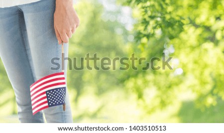 independence day, celebration, patriotism and holidays concept - close up of woman legs and hand holding american flag at 4th july over green natural background