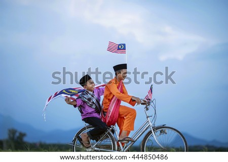 Independence Day concept - Two happy young local boy riding old bicycle at paddy field holding a Malaysian flag