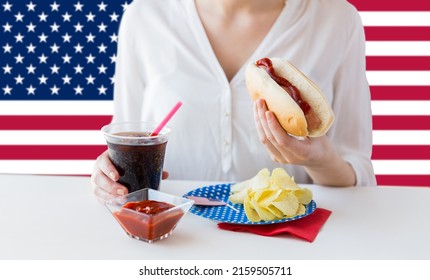independence day, patriotism and holidays concept - close up of woman eating hot dog and drinking cola at 4th july at party over flag of united states of america on background