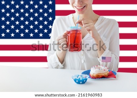 independence day, patriotism and holidays concept - close up of happy woman with iced donut drinking juice from mason jar glass at 4th july party over flag of united states of america on background