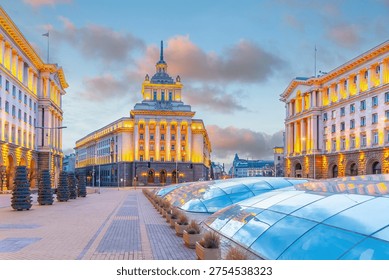 Independence Square in Sofia Bulgaria, featuring the Socialist Classicism architecture of the Party House and government buildings illuminated at sunset.