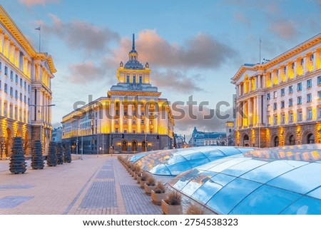 Independence Square in Sofia Bulgaria, featuring the Socialist Classicism architecture of the Party House and government buildings illuminated at sunset.