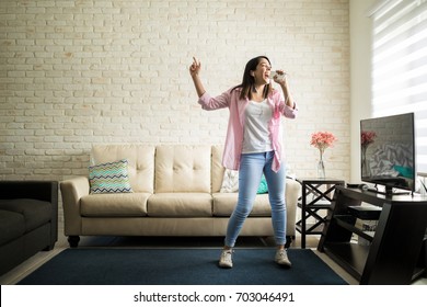 Independent woman singing karaoke alone in her apartment and having fun in the living room