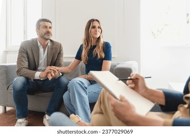 In-depth couple therapy: A young married couple, their faces and emotions in clear focus, share their journey, therapist's notebook, in the foreground, captures the essence of their counseling session - Powered by Shutterstock