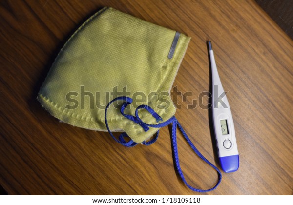 India - May 2, 2020: yellow corona\
virus mask and white thermometer, on a wooden\
background