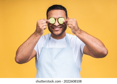 Indian African American Young Man Holding Cucmber Slices Over Eyes And Smile Or Laugh. Isolated Over Yellow Background. Cook Prepaing Food.