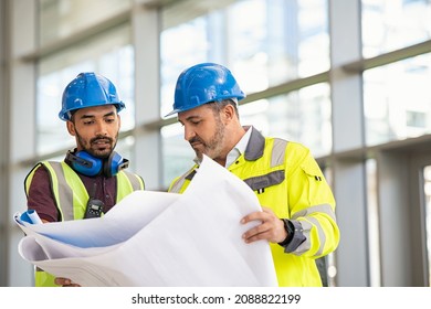 Indian architect and mature supervisor meeting at construction site. Multiethnic manual worker and engineer discussing on plan. Two construction workers working together while visiting a new building.