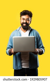 Indian Asian Bearded Young Man In Casual Cloths Using Laptop While Standing Against Yellow Background