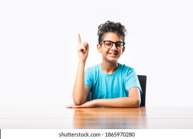 Indian Asian Boy Or Male Child Sitting At Table Or Desk, Looking At Cemara, Thinking Or Pointing Something