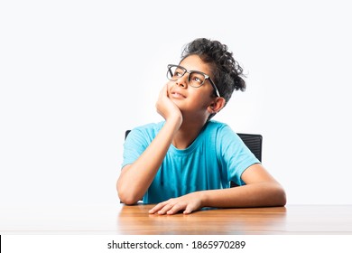 Indian asian boy or male child sitting at table or desk, looking at cemara, thinking or pointing something