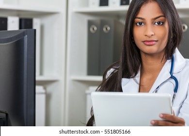 An Indian Asian Female Medical Doctor In A Hospital Office With Stethoscope Using Tablet Computer
