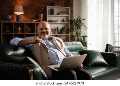 Indian asian handsome senior retired old man using smartphone or laptop while sitting on sofa - Powered by Shutterstock