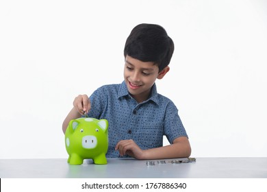 Indian, Asian Kid 6-7 Years Boy Saving Money By Putting It In Pig Shape Piggy Bank, Smiling, Hugging And Thinking