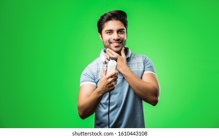 Indian / Asian Man Shaving Beard With Electric Trimmer Or Clipper Standing Isolated Over Green Background