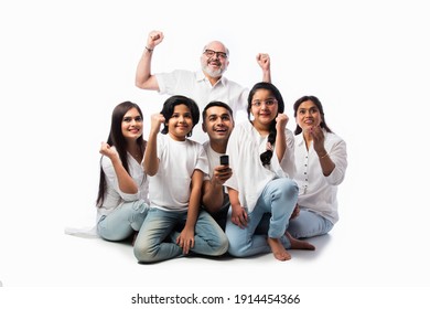 Indian Asian Multigenerational Family Of Six Watching TV Together At Home And Having Fun , Sitting On Floor Against White Background