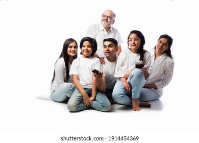 Indian Asian Multigenerational Family Of Six Watching TV Together At Home And Having Fun , Sitting On Floor Against White Background