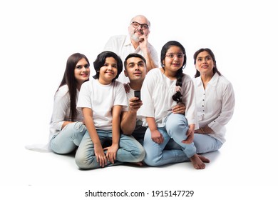 Indian Asian Multigenerational Family Of Six Watching TV Together At Home And Having Fun , Sitting On Floor Against White Background