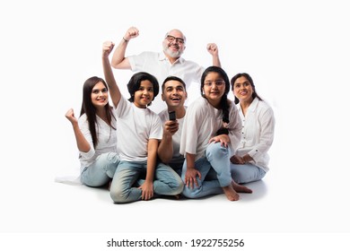 Indian Asian Multigenerational Family Of Six Watching TV Together At Home And Having Fun , Sitting On Floor Against White Background