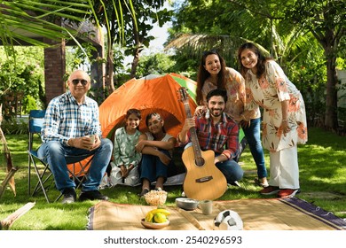 Indian Asian multigenerational family of six camping outdoors, enjoying music, singing, and capturing moments with a selfie, creating joyful memories together - Powered by Shutterstock