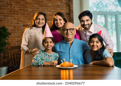 Indian Asian multigenerational family of six celebrating elderly father’s birthday at home with cake, candles, and joyful moments shared across generations - Powered by Shutterstock