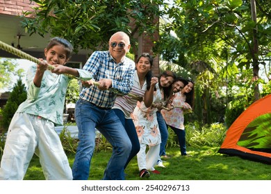 Indian Asian multigenerational family of six camping outdoors, enjoying a fun game of tug of war or Rassi Khech together, creating joyful moments in nature - Powered by Shutterstock