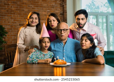 Indian Asian multigenerational family of six celebrating elderly father’s birthday at home with cake, candles, and joyful moments shared across generations - Powered by Shutterstock