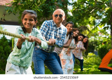 Indian Asian multigenerational family of six camping outdoors, enjoying a fun game of tug of war or Rassi Khech together, creating joyful moments in nature - Powered by Shutterstock