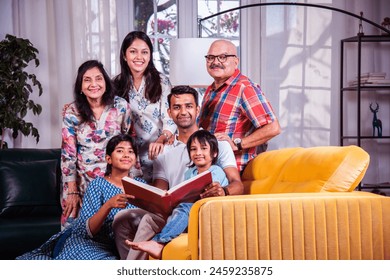 Indian asian multigenerational family watching photos in album or reading book while sitting on sofa together - Powered by Shutterstock