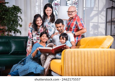 Indian asian multigenerational family watching photos in album or reading book while sitting on sofa together - Powered by Shutterstock