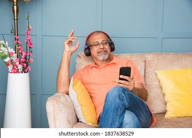 Indian Asian Old Man Using Headphones While Listning To Music Or Watching Movies On Tablet Computer Or Smartphones