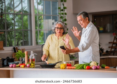 Indian asian retired old age couple using smartphone while cooking meal in kitchen together - Powered by Shutterstock