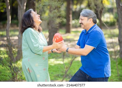 Indian Asian Senior Man Give Heat Shape Balloon To Woman At Park, Love And Happiness Concept, Old Couple In Love Having Fun, Elderly Husband And Wife Together Celebrating Valentine's Day Outdoor.