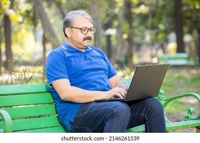 Indian asian senior man sitting on bench using laptop at park. Old or mature people wearing eye glasses using computer, modern technology concept. - Powered by Shutterstock