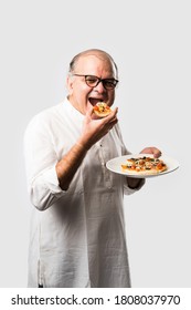 Indian Asian Senior Or Old Man Eating Pizza While Standing Isolated Against White Background