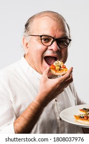 Indian Asian Senior Or Old Man Eating Pizza While Standing Isolated Against White Background