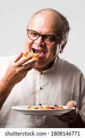 Indian Asian Senior Or Old Man Eating Pizza While Standing Isolated Against White Background