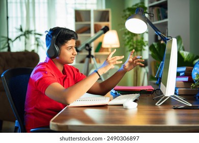 Indian Asian teenage boy studying using computer, headphones, smartphone for online class, homework - Powered by Shutterstock