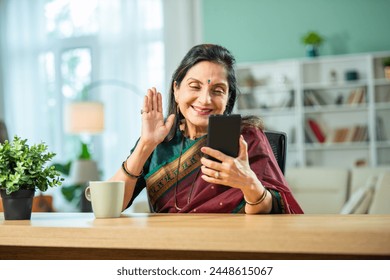 Indian asian woman in 60s  using smartphone at home, sitting at breakfast table - Powered by Shutterstock