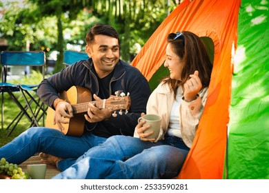 Indian Asian young couple or friends enjoying a laid-back camping trip, sipping coffee, reading a book, or playing guitar. They laugh and share fun moments in the fresh outdoors, creating memories - Powered by Shutterstock