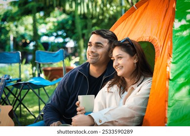 Indian Asian young couple or friends enjoying a laid-back camping trip, sipping coffee, reading a book, or playing guitar. They laugh and share fun moments in the fresh outdoors, creating memories - Powered by Shutterstock