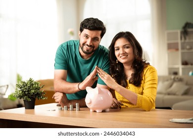 Indian asian young couple and saving concept putting coins in piggy bank at home - Powered by Shutterstock