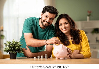 Indian asian young couple and saving concept putting coins in piggy bank at home - Powered by Shutterstock